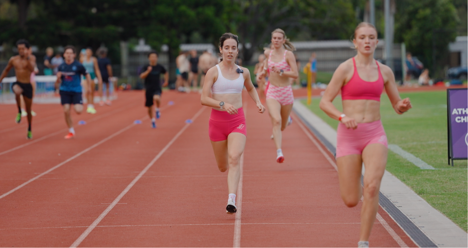 Athletes running on a track with trees and stadium seats in the background