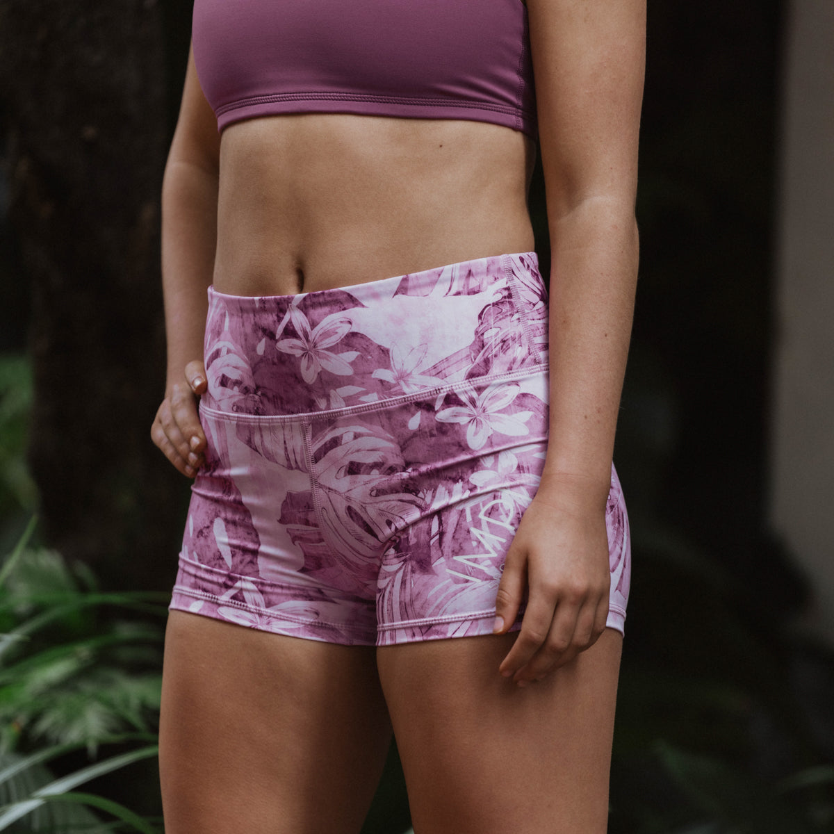 Person wearing pink athletic shorts with a floral pattern against a blurred natural background