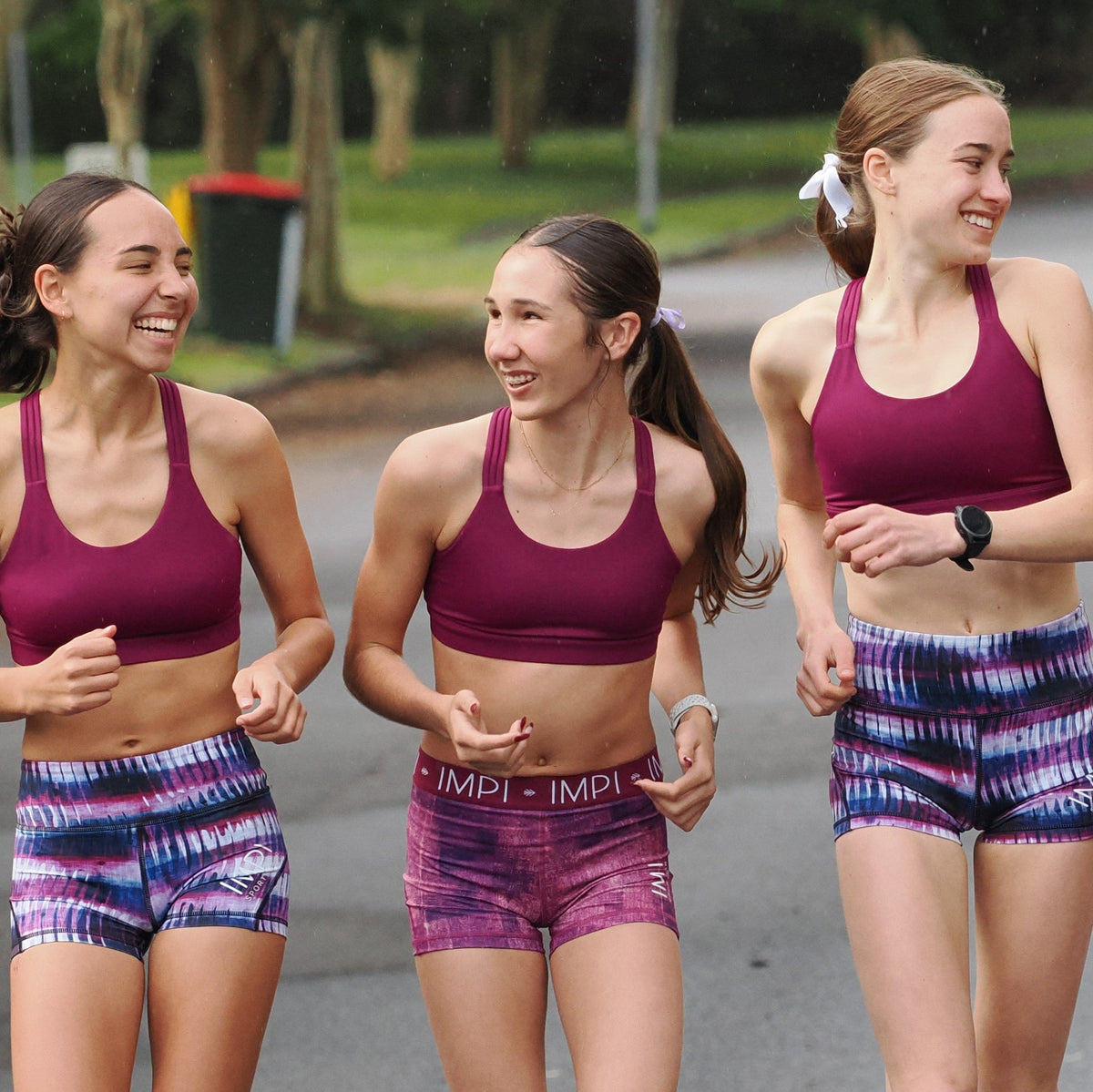 Three women in athletic wear running outdoors on a paved path.