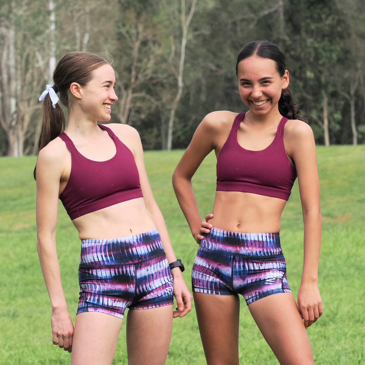 Two women wearing matching athletic outfits in a grassy outdoor setting