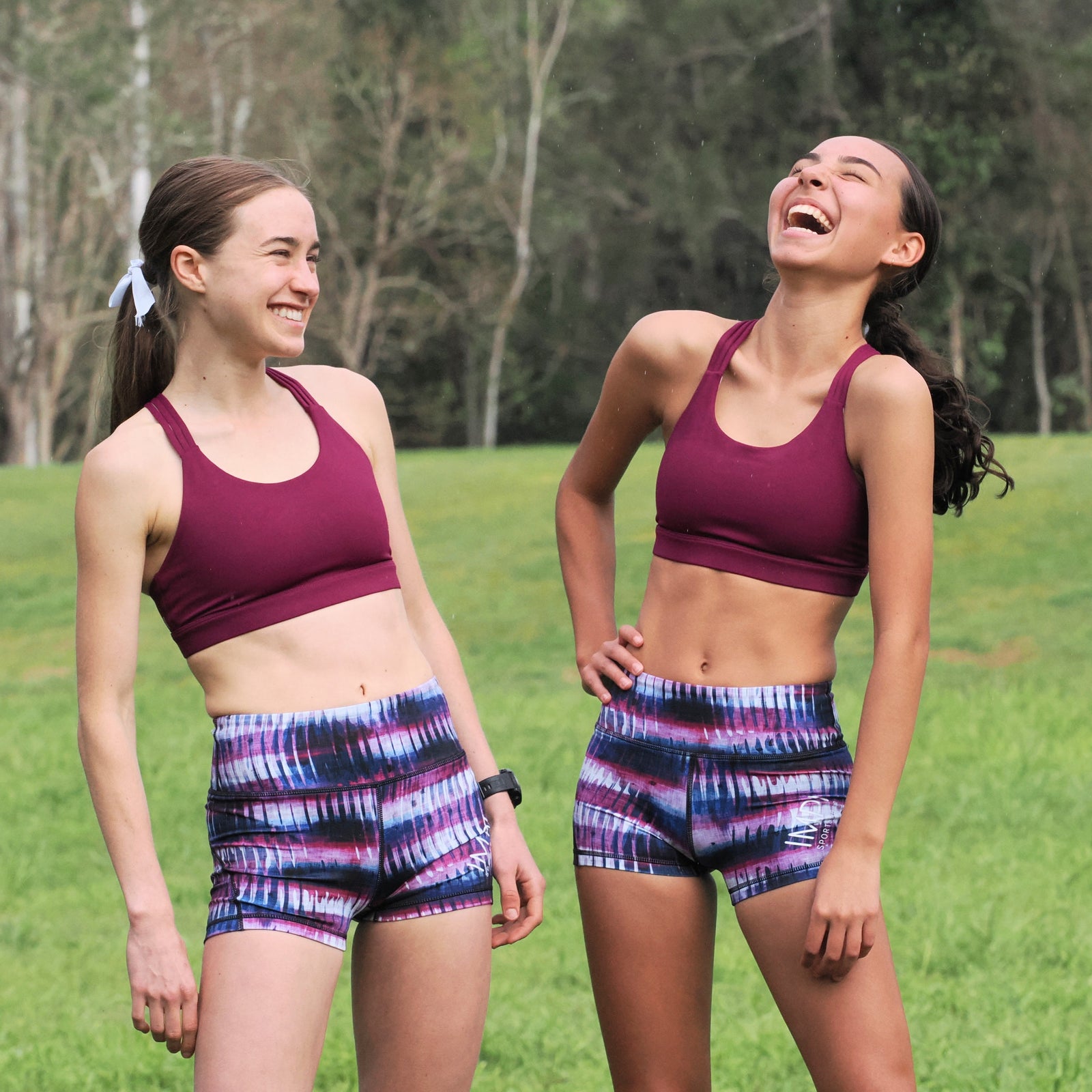 Two women in matching athletic wear standing in a grassy outdoor setting.