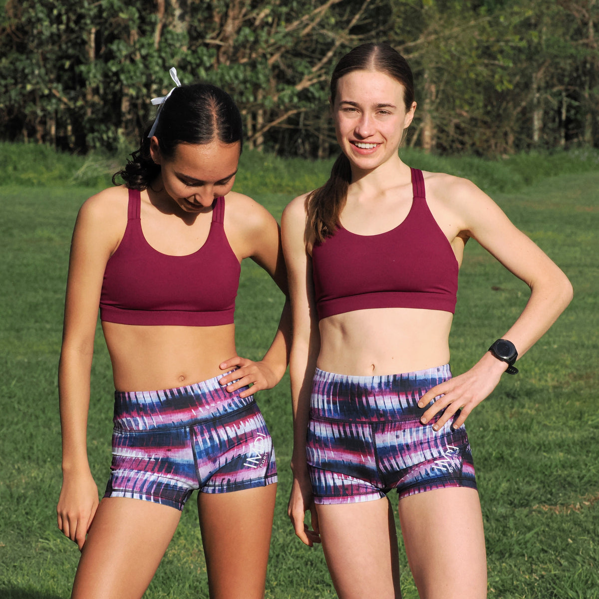 Two women wearing matching athletic outfits standing in a grassy outdoor area.